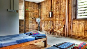 A room with a bed, two wicker chairs, a fan, and a window with blinds. - Borneo Tribal Village (Kuching)