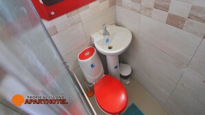 Um banheiro pequeno com pia branca, vaso sanitário vermelho e lixeira vermelha.