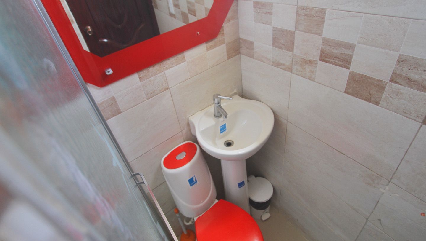 Un baño pequeño con lavamanos blanco, inodoro rojo y un cubo de basura rojo.