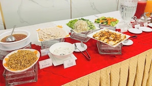 Een buffettafel met diverse gerechten, waaronder noedels, salade en een kom soep.