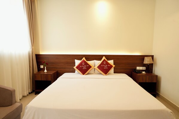 A hotel room with a neatly made bed, two decorative pillows, a bedside table with a lamp, and a nightstand with a phone.
