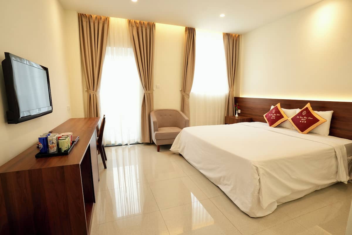 Une chambre d’hôtel avec un lit, un bureau avec une télévision et des rideaux.