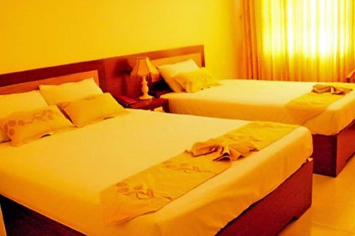 Une chambre d’hôtel avec deux lits, chacun doté d’une tête de lit en bois, d’une table de chevet et d’une lampe.