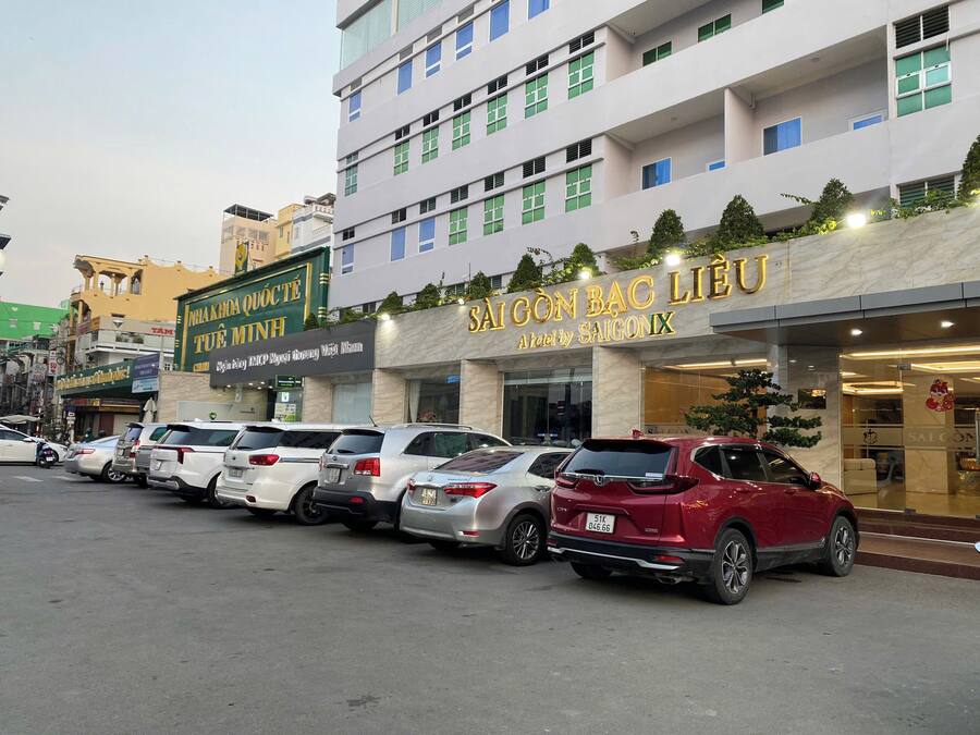Un hotel con fachada moderna, varios pisos y una fila de coches estacionados al frente.