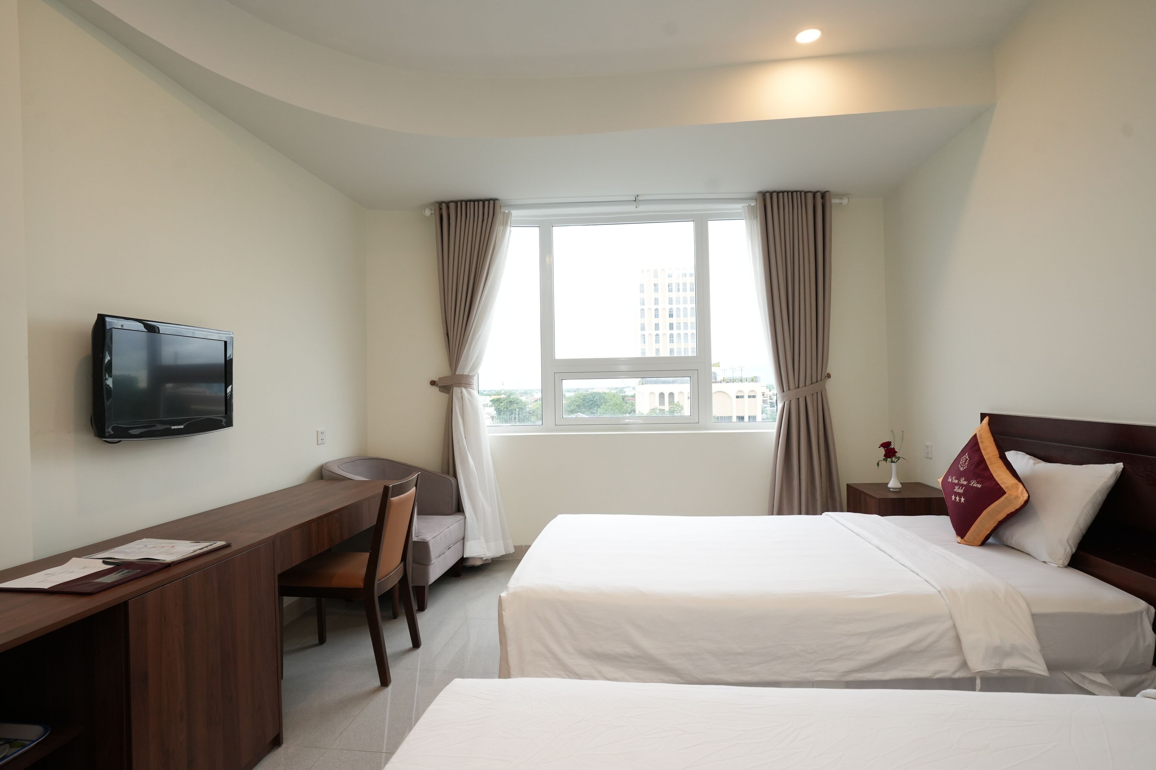 Habitación de hotel con cama, escritorio, silla, televisor y ventana con cortinas.