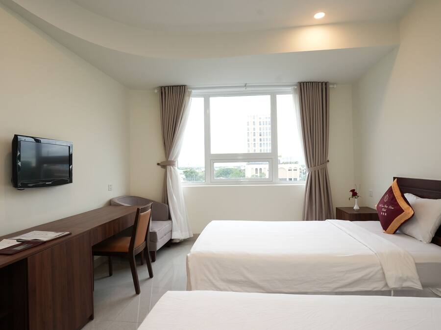Habitación de hotel con cama, escritorio, silla, televisor y ventana con cortinas.