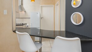 Cozinha moderna com bancada preta, cadeiras brancas e coifa de aço inoxidável.