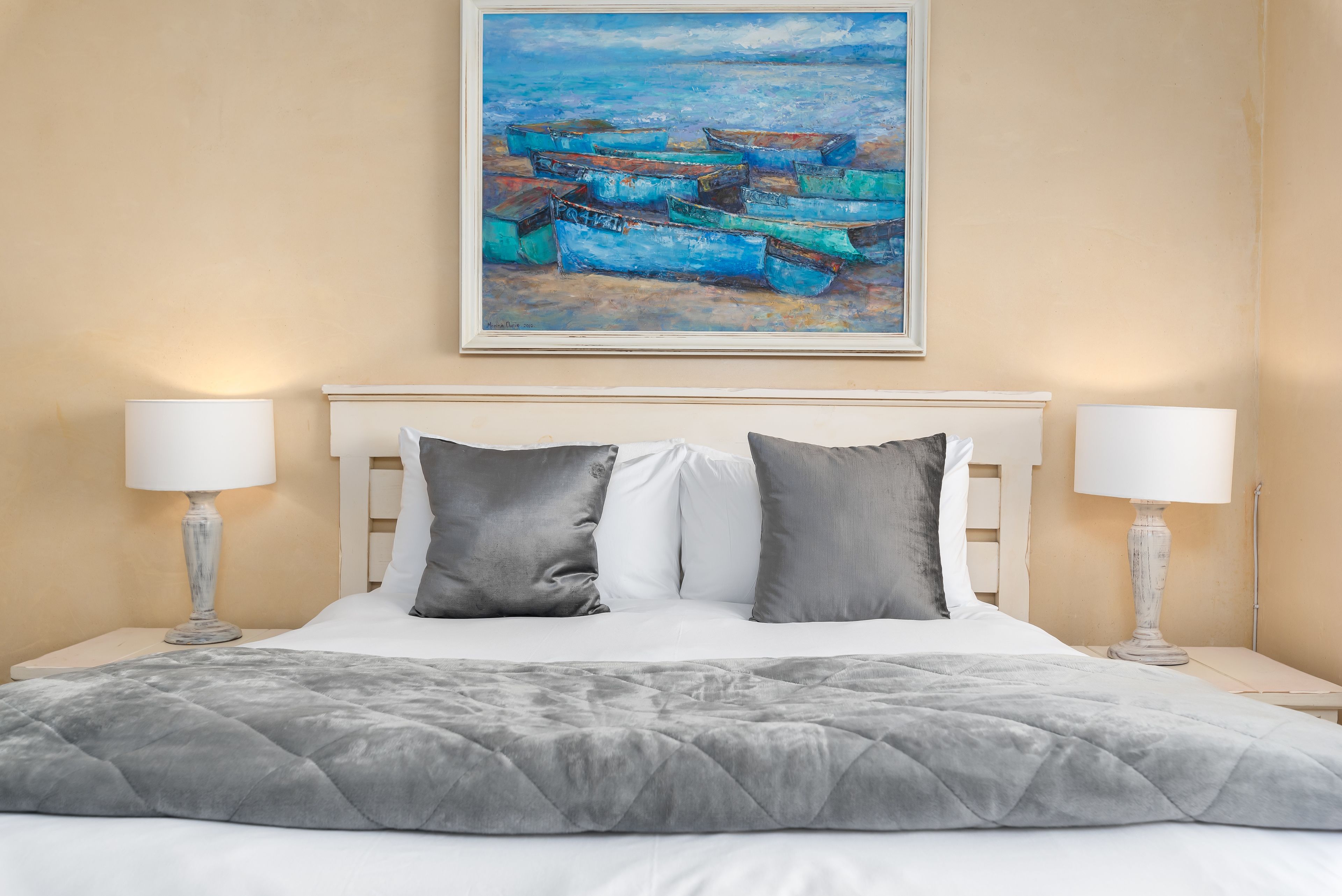 Una cama bien hecha con colcha gris, almohadas blancas y dos lámparas de noche.