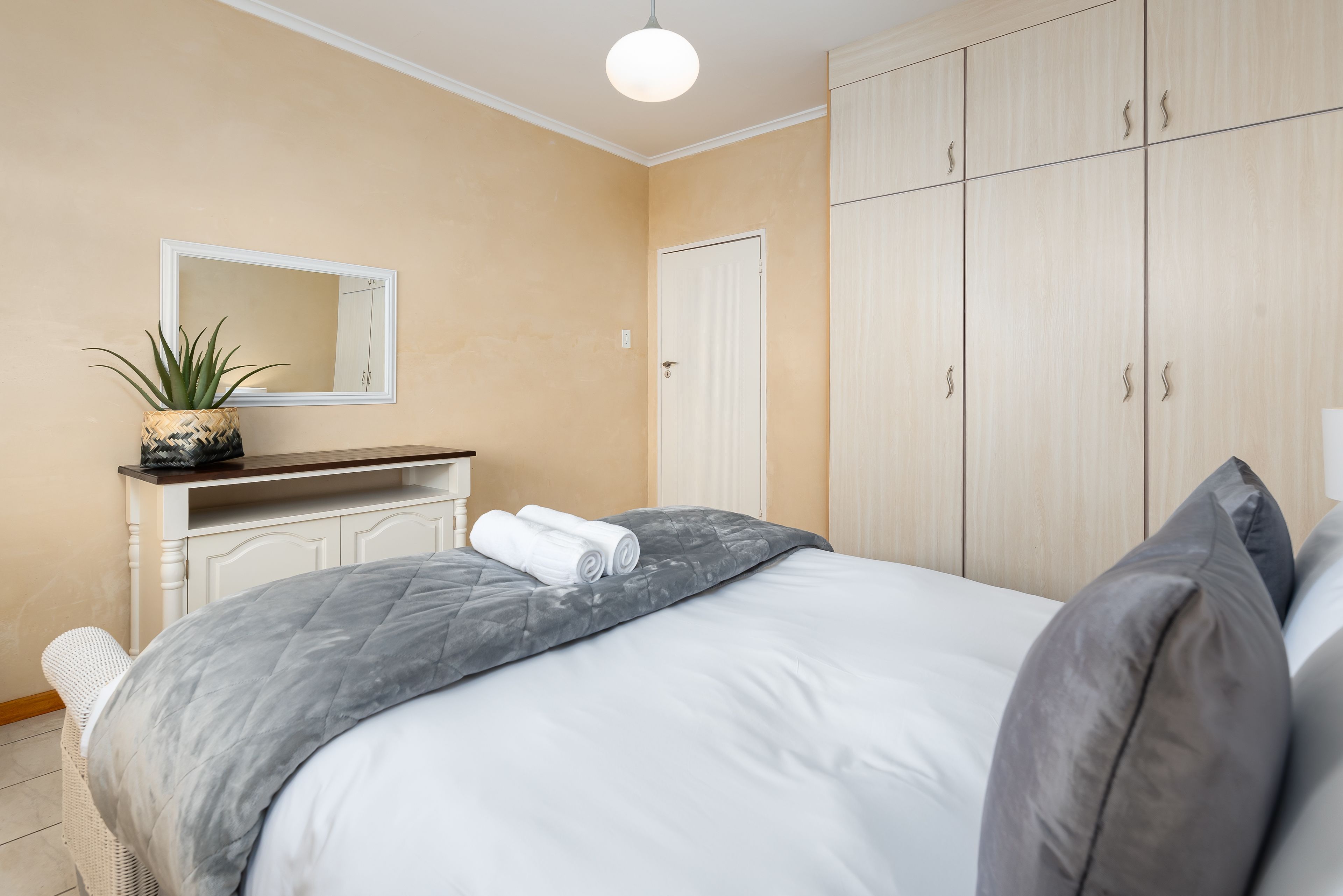 A bedroom with a bed, a bedside table, a mirror, a wardrobe, and a potted plant.