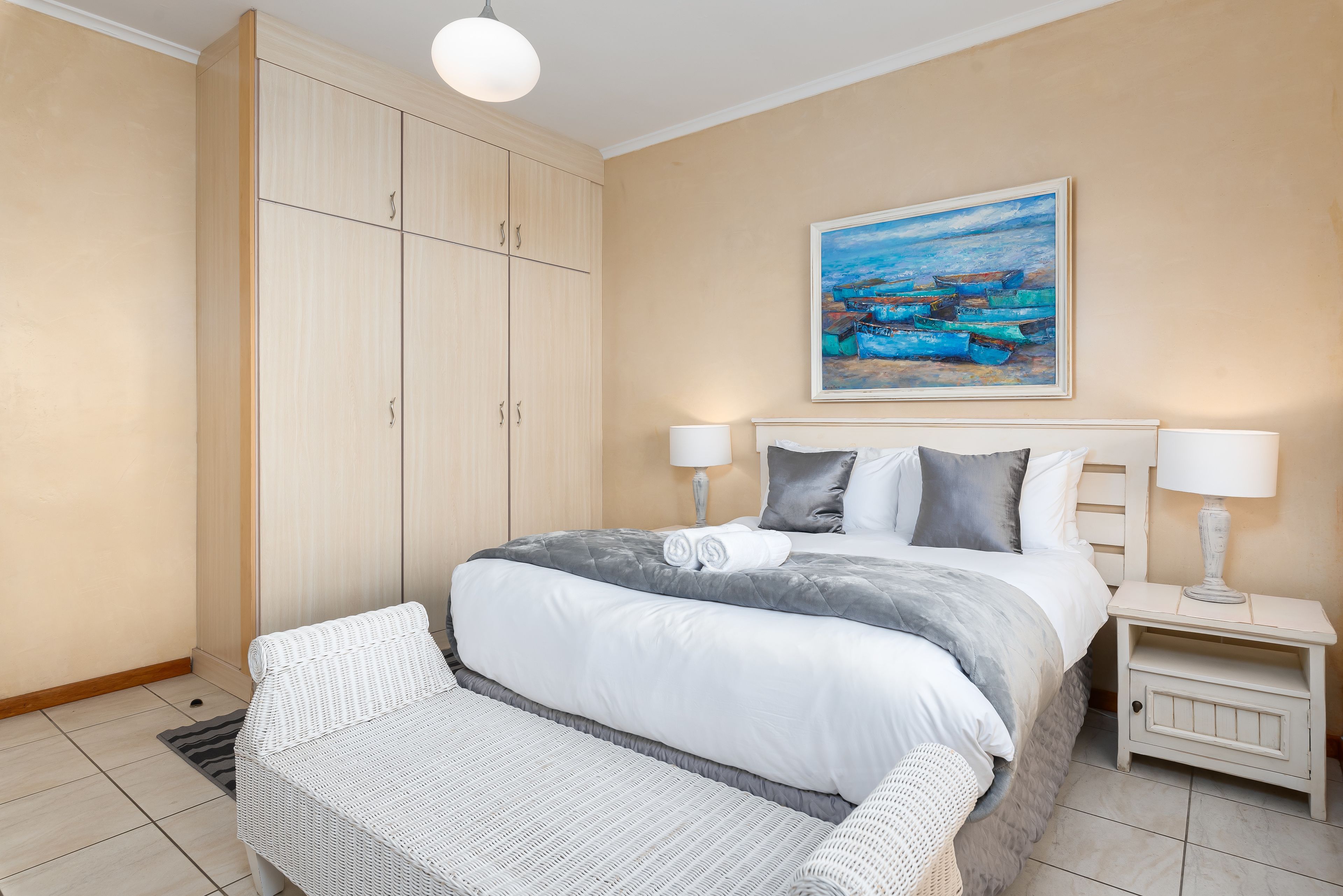 Une chambre bien rangée, avec un grand lit, des tables de chevet et un tableau accroché au mur.