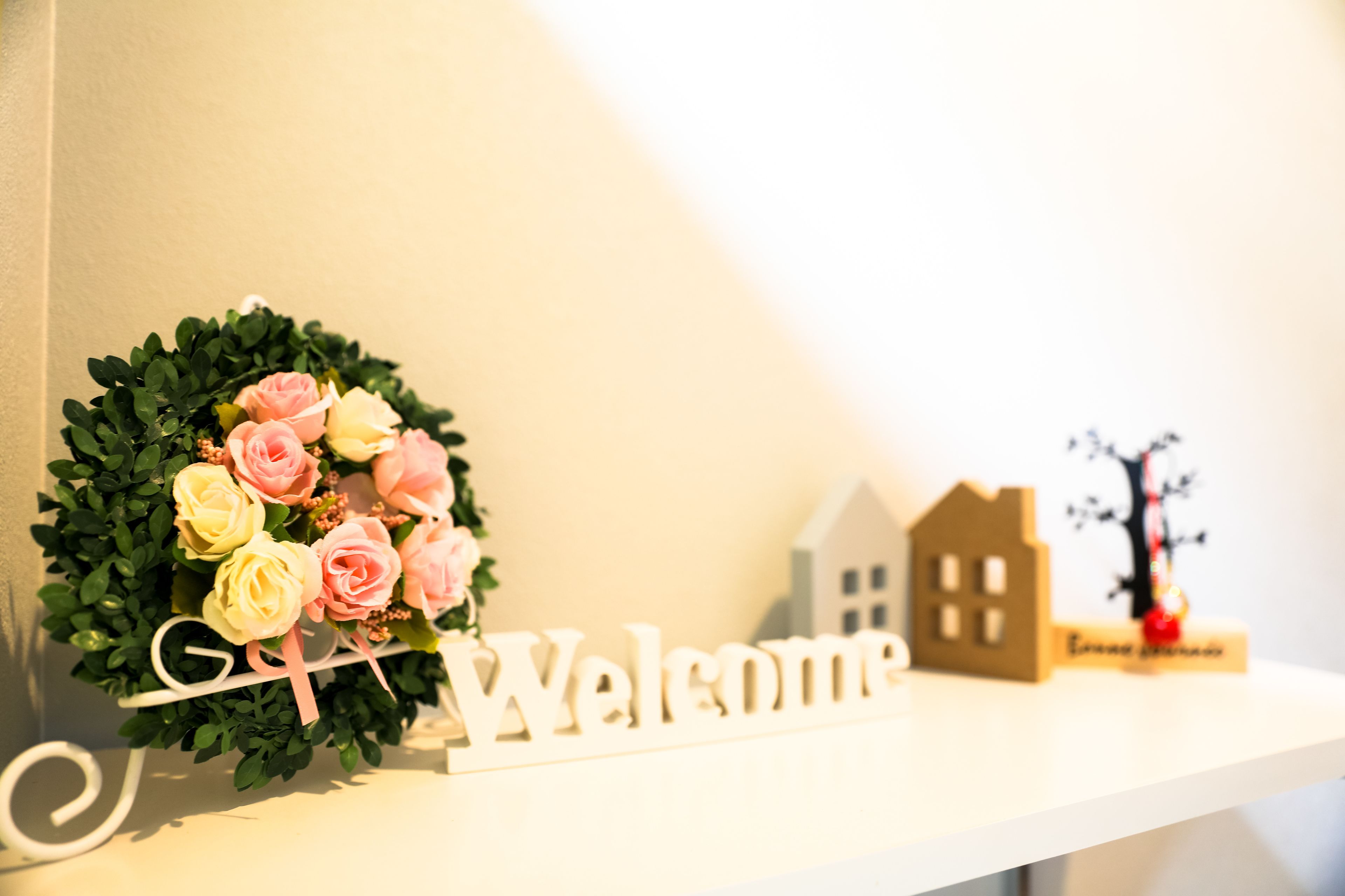 A welcome sign with a wreath of pink and yellow roses on a white shelf.