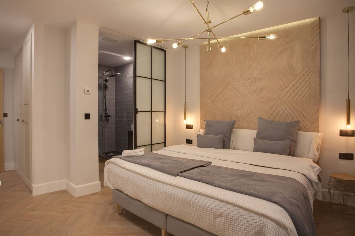 Un dormitorio moderno con una cama grande, lámparas de noche y un cabecero de madera.