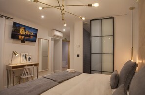 A modern bedroom with a large bed, a desk, a chair, and a TV mounted on the wall. - Suites You Soho (Madrid)