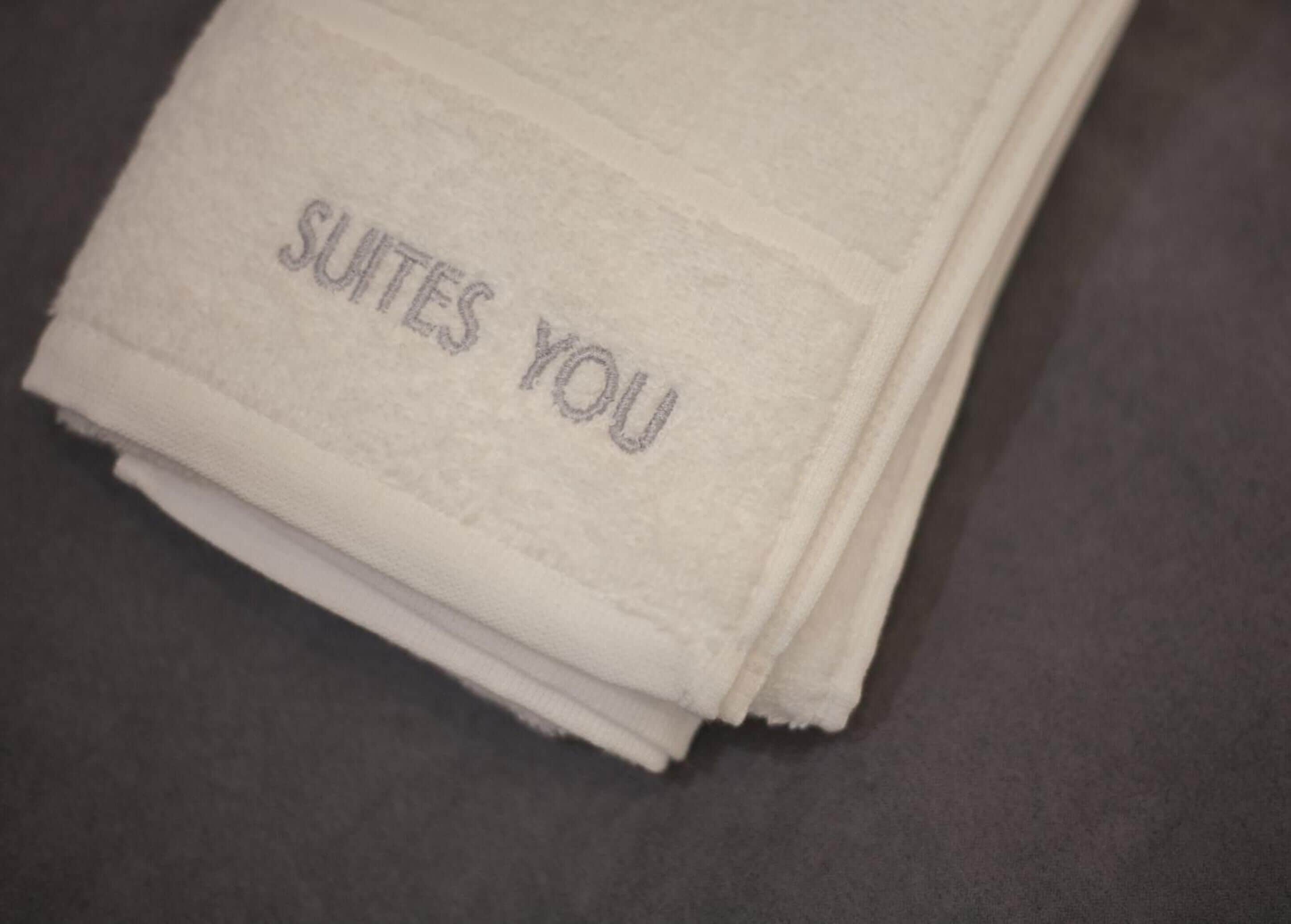 Een stapel witte handdoeken met de tekst 'SUITES YOU' erin gestanst.