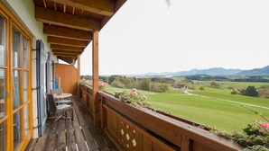 Een houten balkon met uitzicht op een groen veld en bergen.