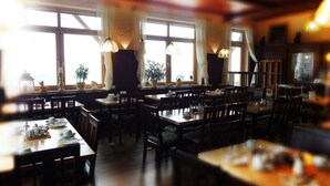 Een restaurant met meerdere tafels en stoelen, grote ramen met gordijnen en hangende lampen.
