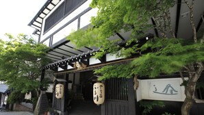 A traditional Japanese building with a covered entrance, potted plants, and hanging lanterns.