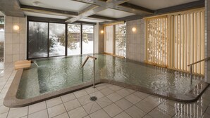 A modern indoor swimming pool with clear water, wooden railings, and a tiled floor.
