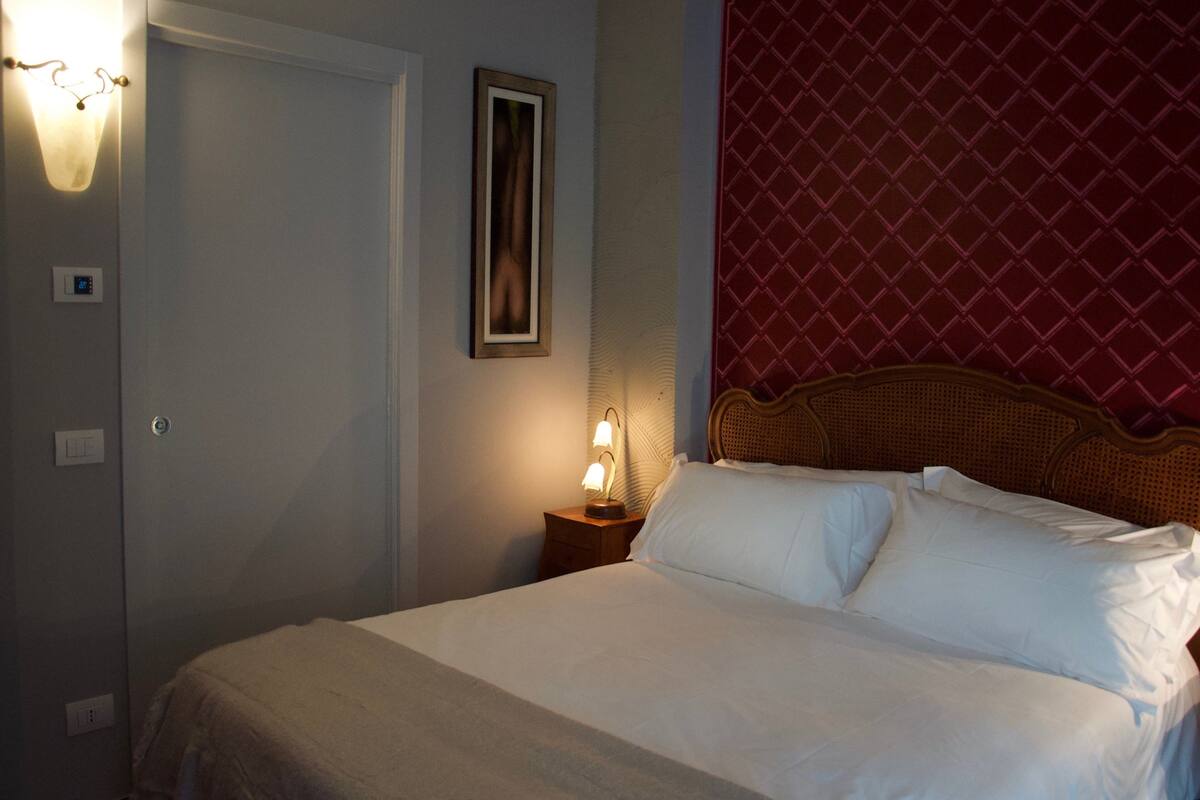 A neatly made bed with white linens, a bedside lamp, and a framed picture on the wall.