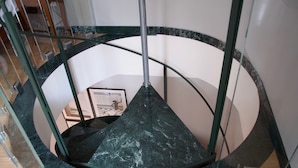A spiral staircase with a glass railing and a dark marble floor. - Residenza Diana (Toscolano Maderno)