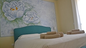 A hotel room with a bed, a teal headboard, and a large floral painting on the wall. - Residenza Diana (Toscolano Maderno)