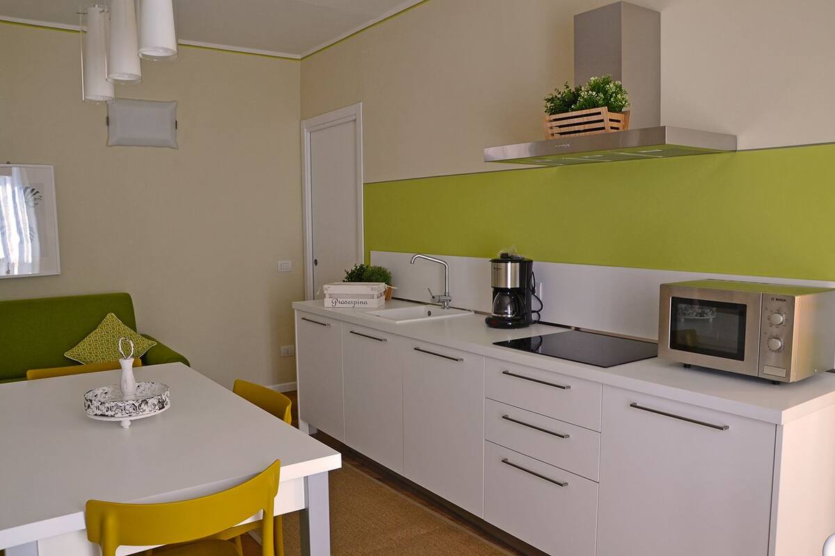 A compact kitchen with a white countertop, a Bosch microwave, a coffee maker, and a small sink.