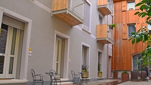 A courtyard with outdoor seating, a wooden deck, and a building with balconies. - Residenza Diana (Toscolano Maderno)
