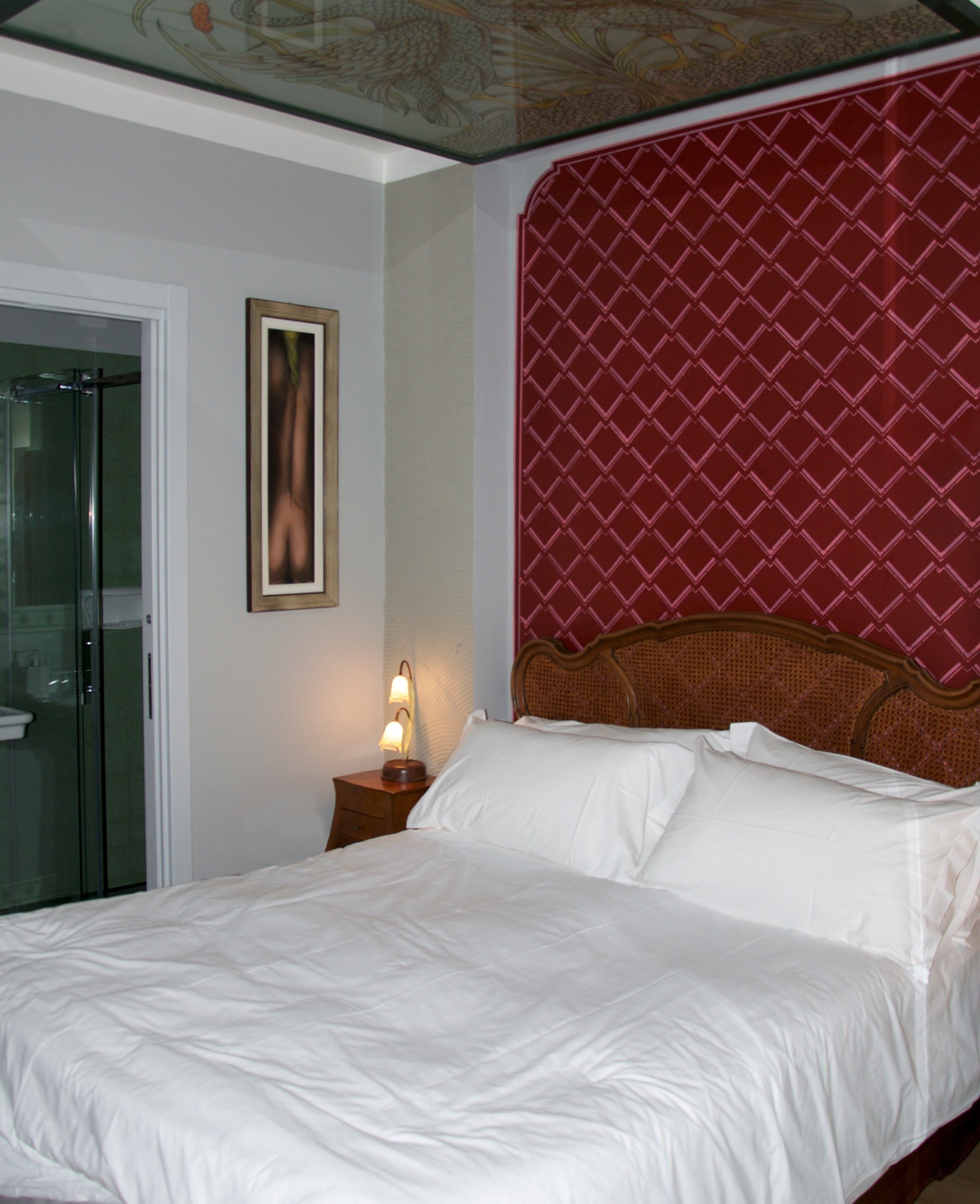 A hotel room with a bed, a nightstand with a lamp, a door, and a wall with a patterned design.