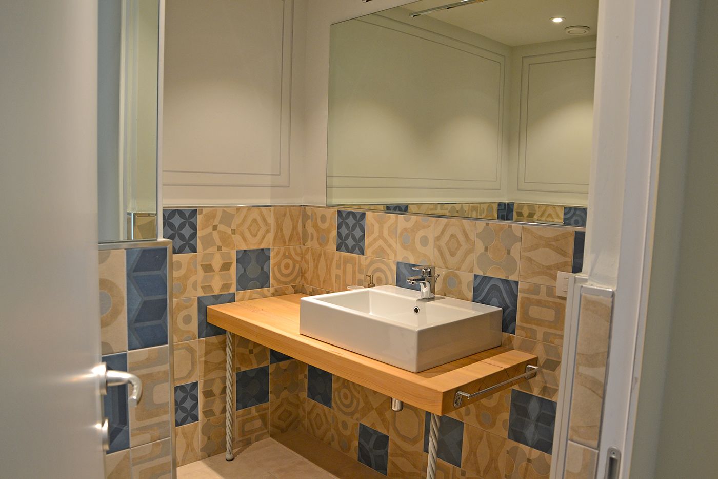 A bathroom with a rectangular sink, patterned tiles, and a wooden countertop.