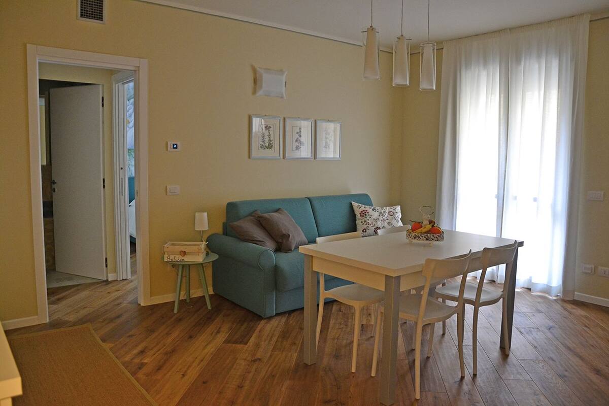 A cozy living room with a teal sofa, a white dining table, and a small side table with a lamp.