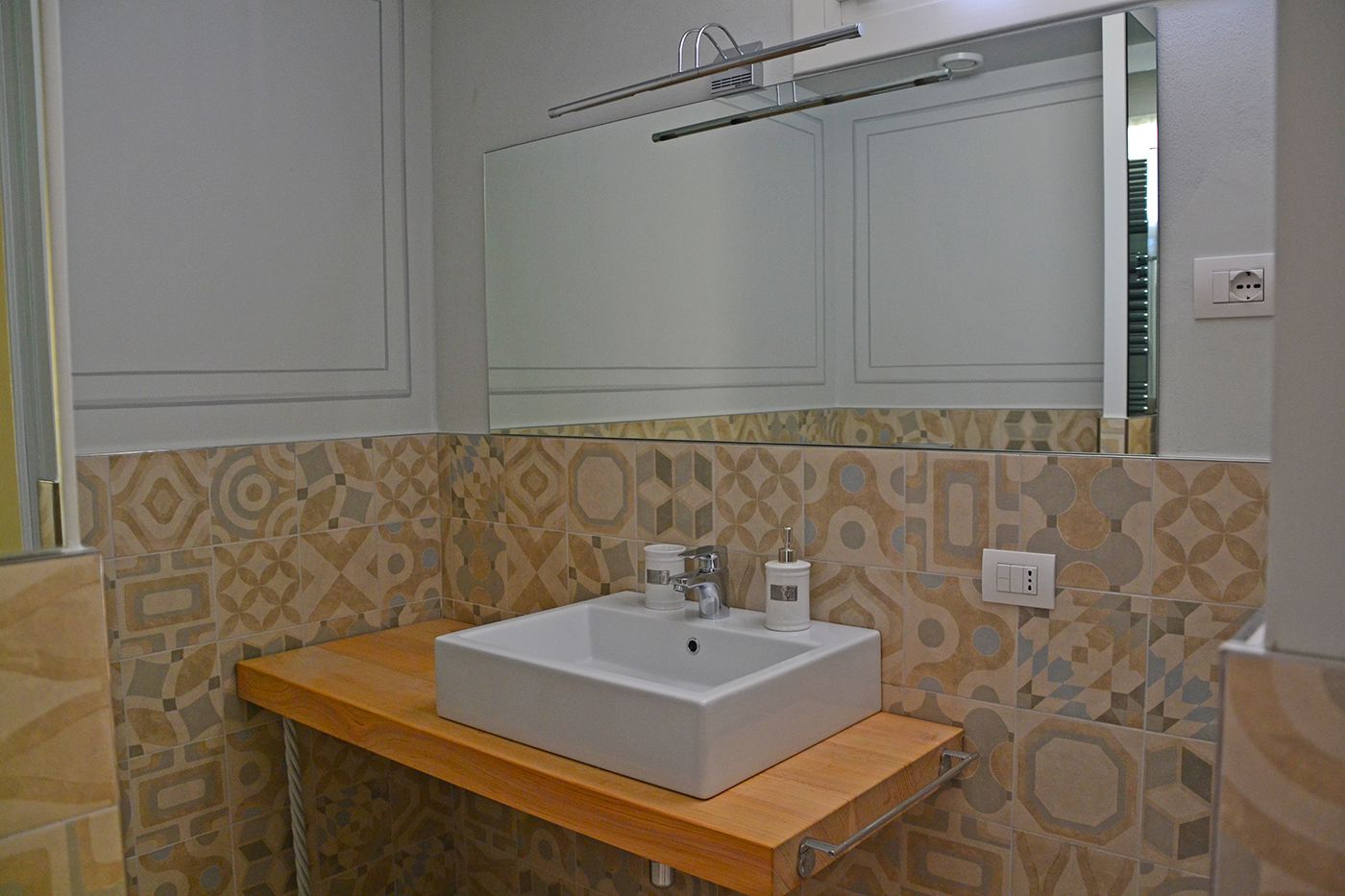 Une salle de bain avec un lavabo blanc, un plan de toilette en bois et des carreaux décorés.