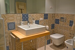 Une salle de bain avec un lavabo rectangulaire, des toilettes et un bidet. Les murs sont recouverts de carreaux aux motifs géométriques.