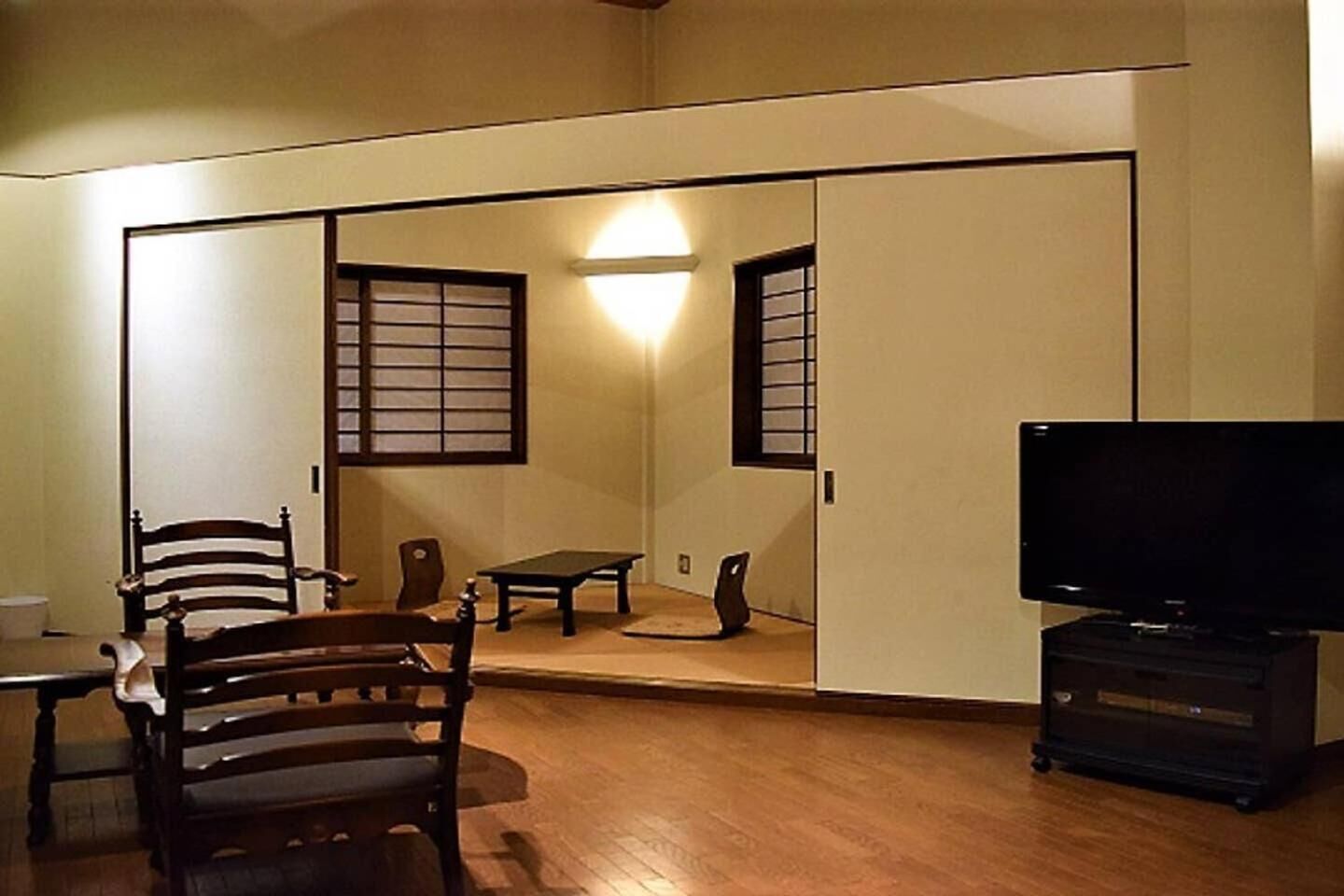 A traditional Japanese-style room with sliding doors, a television, a table, and chairs.
