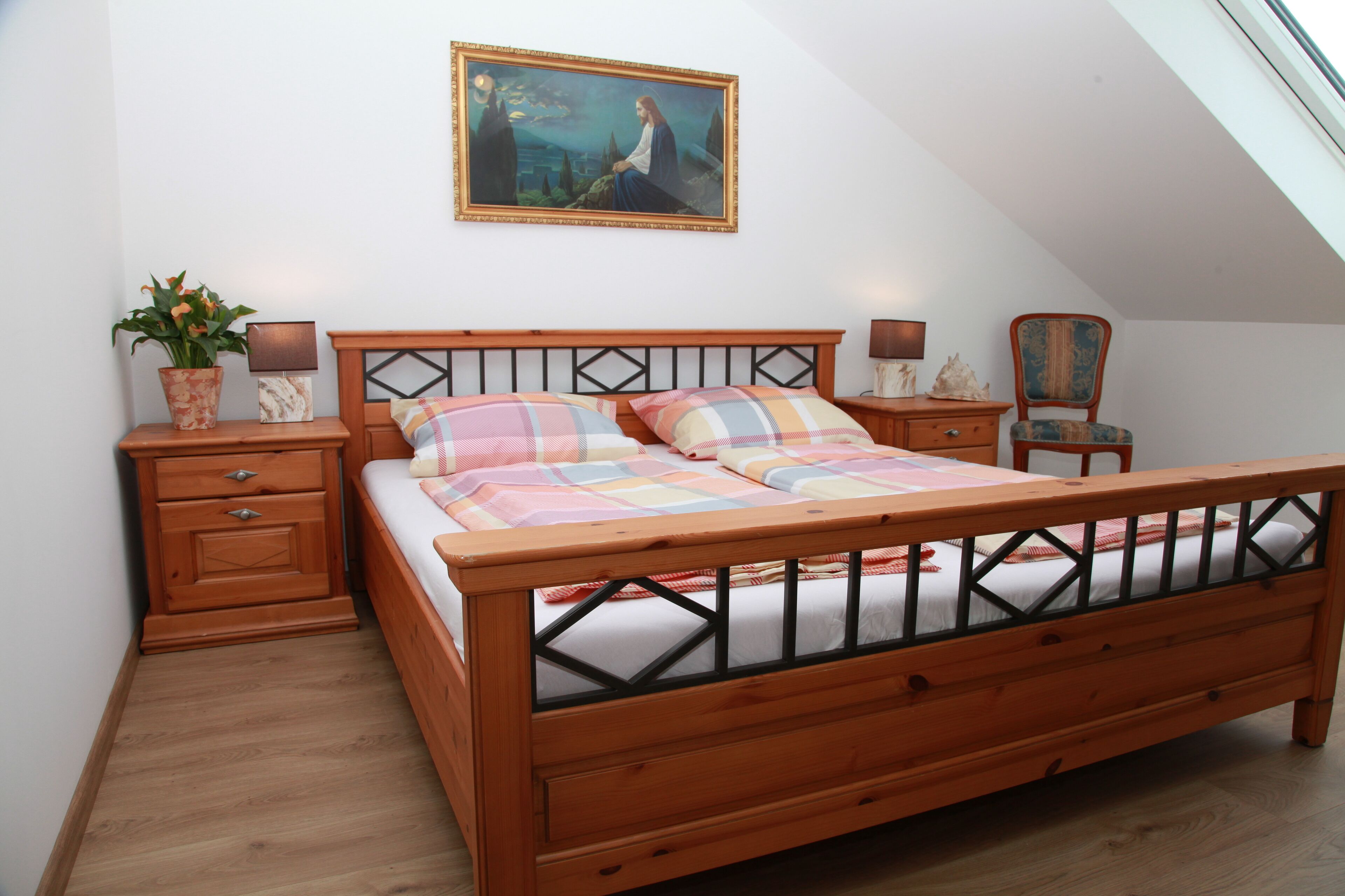 A bedroom with a wooden bed, a nightstand, a chair, a painting on the wall, and a window.