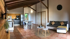A spacious living area with a sofa, a dining table with chairs, a kitchen in the background, and a large window.