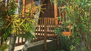 A wooden building with a red roof, surrounded by lush greenery including palm trees and other tropical plants.