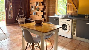 A kitchen with a washing machine, wooden wall shelves, a hanging chair, and a dining table.