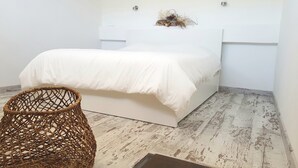 Ein Schlafzimmer mit einem weißen Bett, einem gewebten Sessel und einem rustikalen Holzboden.