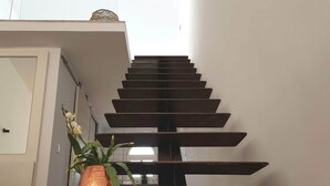 Eine moderne, minimalistisch gestaltete Treppe führt zu einem hellen Raum mit einer weißen Tür und einem Blumentopf.