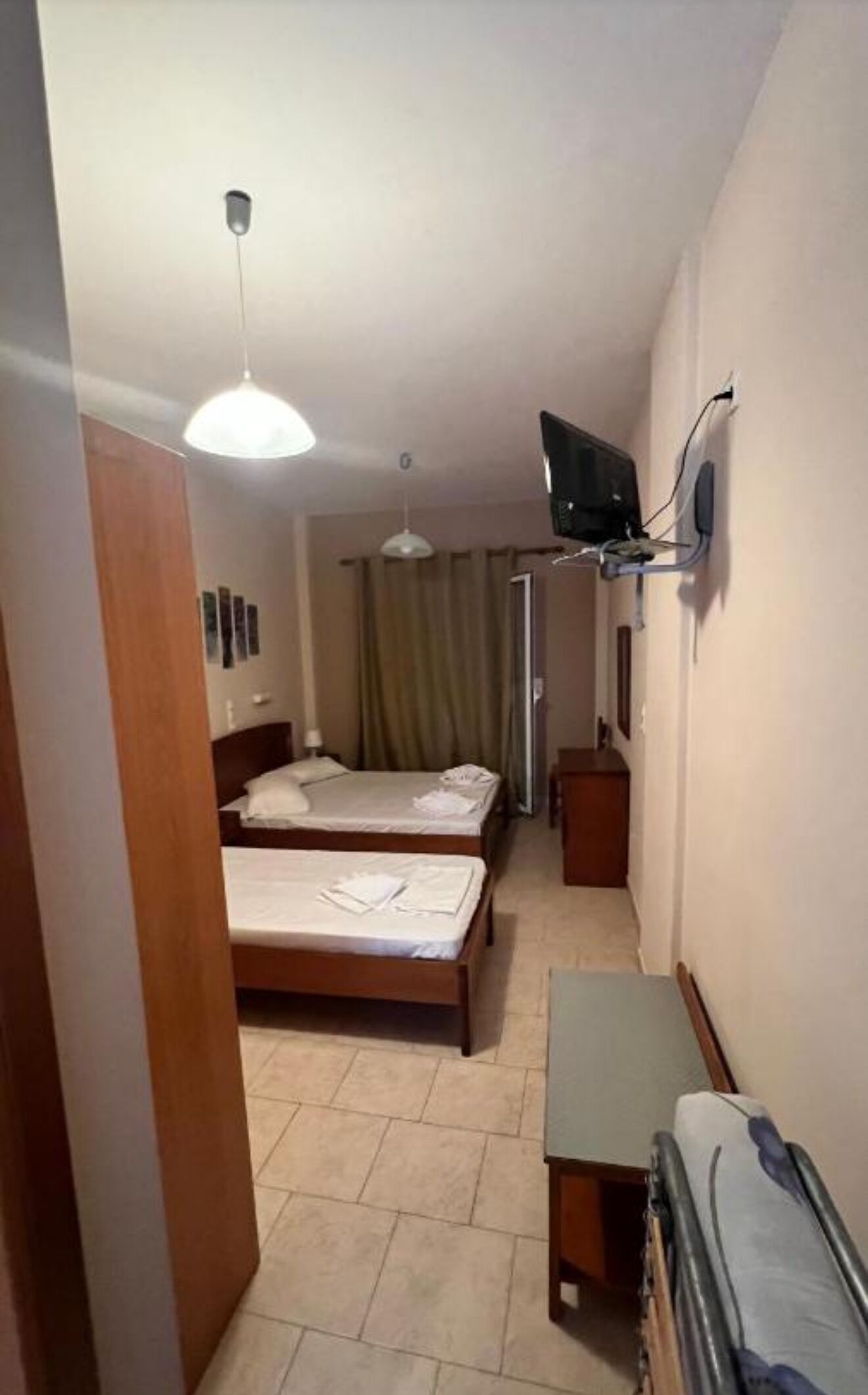 Habitación de hotel con dos camas individuales, un televisor montado en la pared, una mesita pequeña y un ventilador de techo.