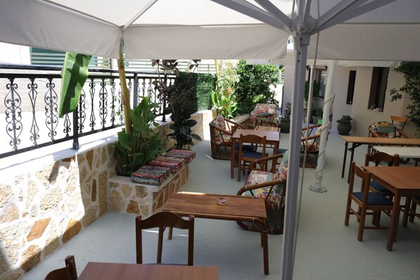 Un patio exterior con paredes de piedra, mesas y sillas de madera, y plantas en macetas.