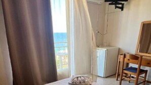 A hotel room with a bed, a desk, a chair, a TV, and a view of the sea. - Michaela (Kefalonia)