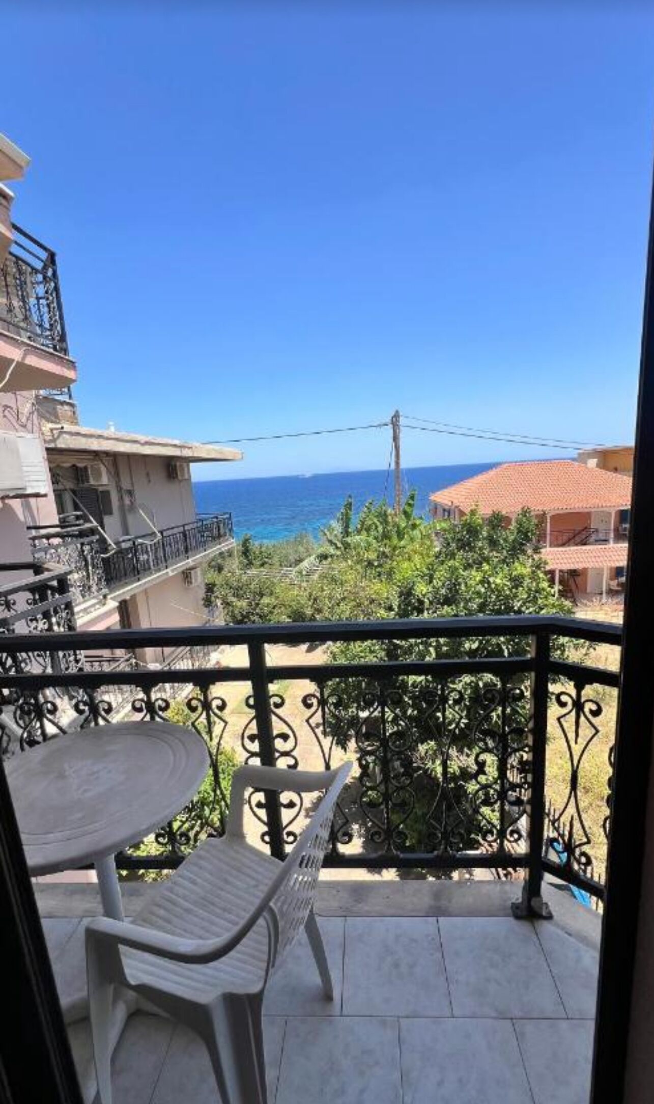 A balcony with a table and chairs, overlooking a residential area and the sea.