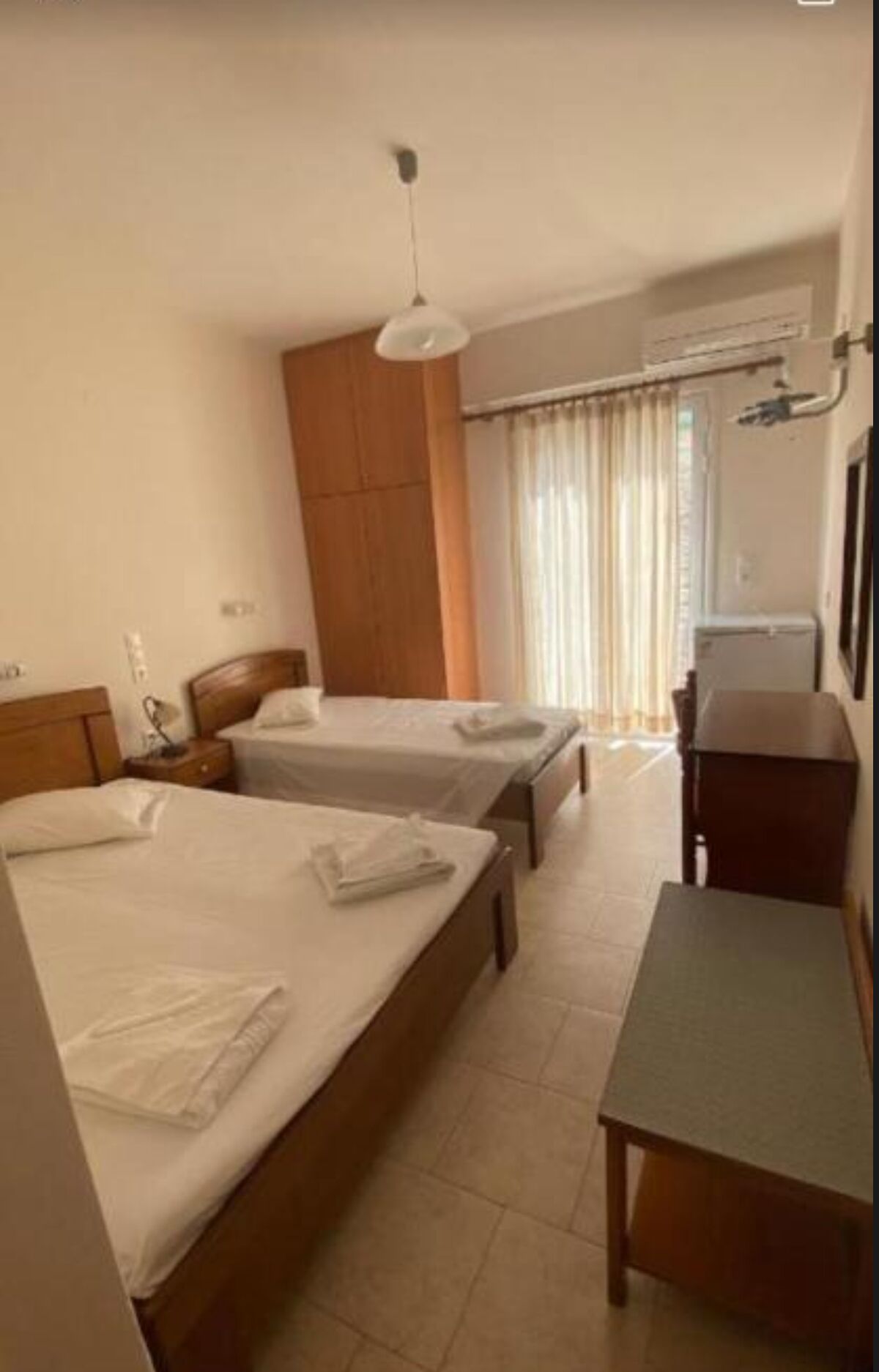 Une chambre d’hôtel avec deux lits, un bureau, une chaise, une armoire et une fenêtre avec des rideaux.