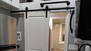 A compact kitchen with a stainless steel refrigerator, white cabinets, a sliding door, a granite countertop, and a sink with a faucet.