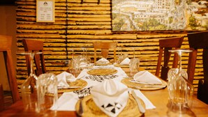 A dining table set with plates, glasses, and cutlery, with a wooden wall and a cityscape painting in the background. - Vintage Cottage (Gishari)