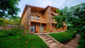 A wooden log cabin with a balcony, surrounded by lush greenery and a stone pathway. - Vintage Cottage (Gishari)