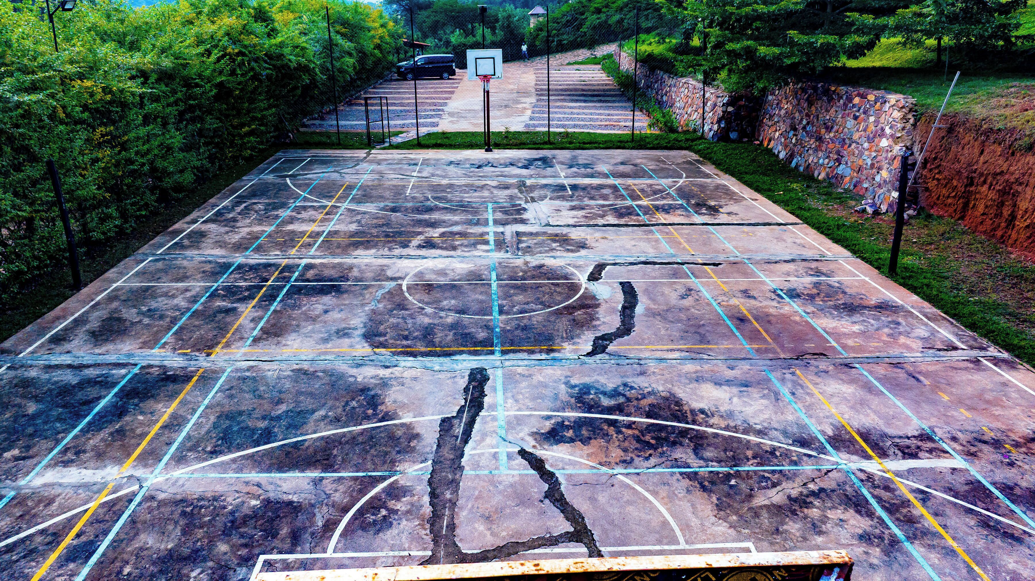 A basketball court with a stone wall and trees in the background.