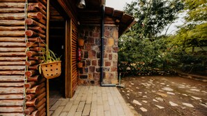 A rustic wooden building with a stone wall entrance, a hanging plant, and a stone pathway leading outside. - Vintage Cottage (Gishari)