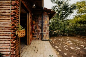 A rustic wooden building with a stone wall entrance, a hanging plant, and a stone pathway leading outside. - Vintage Cottage (Gishari)